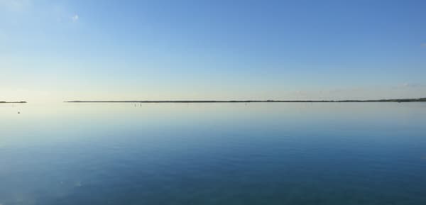 Calm, flat ocean in blue with blue sky only a landline dividing both.